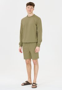Olivgrön sweatshirt och shorts-set i mjukt material, med rund hals och elastisk midja. Bruna sandaler med spänne.