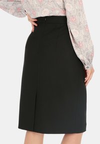 Czarna spódnica o dopasowanym kroju, z tylnym rozcięciem, gładką teksturą i ukrytym zapięciem na zamek z tyłu.