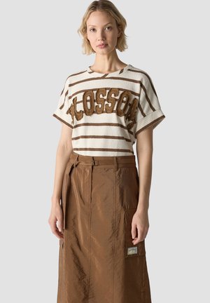 Woman wearing a white and brown striped short-sleeve shirt with "CLOSSOM" text and a high-waisted brown skirt with pockets and belt loops.