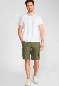 T-shirt blanc à col en V associé à un short cargo vert olive avec deux poches latérales et deux poches arrière, porté avec des baskets blanches.