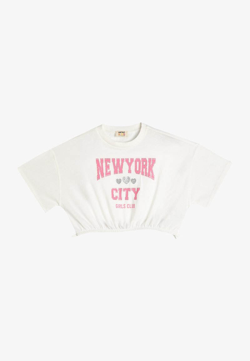 Valkoinen lyhythihainen crop-top, jossa on kootut helmat ja jossa lukee "NEW YORK CITY" vaaleanpunaisella ja harmaalla glitterillä, ja sen alla on teksti "GIRLS CLUB".