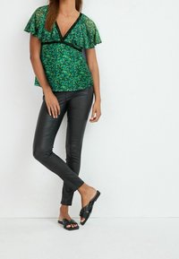 Top verde con stampa floreale, maniche a volant e un accento nero. Abbinato a pantaloni in ecopelle neri aderenti e sandali neri senza tacco.