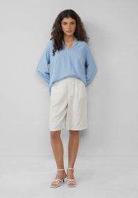 Lichtblauw, lang mouw, V-hals top gecombineerd met witte, gestreepte kniebundlei shorts en witte, bandjes sandalen. Hete gladde textuur.