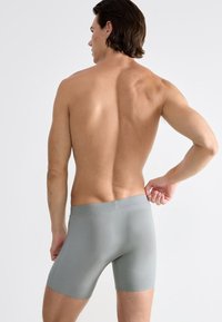 Graue Baumwoll-Boxershorts mit glatter Textur, ausgestattet mit einem nahtlosen Bund, von hinten auf einem männlichen Modell vor einem neutralen Hintergrund gezeigt.