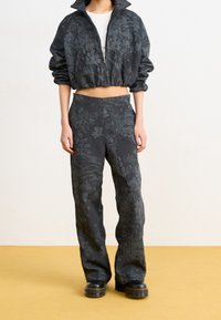 Veste courte noire à imprimé floral avec col montant, associée à un pantalon large noir à motifs floraux. Les deux pièces sont en tissu texturé et ont une coupe décontractée.