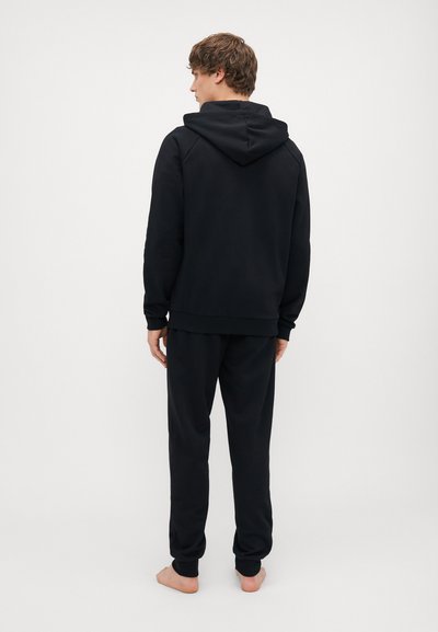 Fekete kapucnis pulóver és melegítőnadrág szett, puha anyagból készült, húzózsinórral ellátott kapucnival, bordás mandzsettákkal és laza szabással. Hátulról látható.