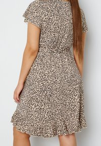 Šaty s leopardím potiskem v béžové a černé barvě, s přiléhavým pasem, krátkými rukávy a rozšířeným lemem s volánkovým detailem.
