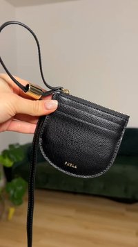 Pochette en cuir noir à finition texturée, dotée d'une fermeture éclair, de fentes pour cartes et d'une bandoulière amovible. Détail logo doré à l'avant.