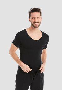 Black short-sleeve V-neck t-shirt made from smooth fabric, fitted design, worn with unfastened black pants, model standing and smiling.
