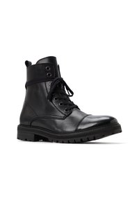 Botas de tobillo negras de cuero con cordones, con una superficie texturada, puntera redonda, suela de goma plana y ojales de metal. Presentan un cuello acolchado.