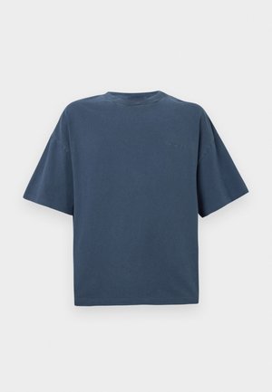 T-shirt oversize à manches courtes bleu marine avec un petit logo Carhartt brodé sur la poitrine gauche sur fond blanc.