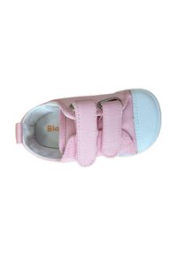Zapato de niña pequeño en color rosa con parte superior de lona, dos correas de Velcro y suela de goma azul clara. El interior tiene un forro suave con marca.