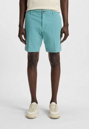 Teal bomuldsshorts med knaplukning, forlommer og rullet kant. Bæret med cremefarvede sneakers og en beige top. Casual design.