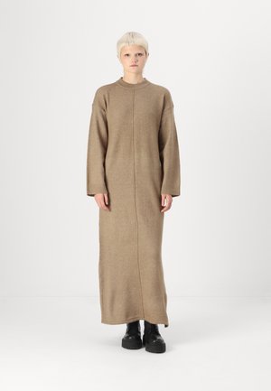 Beige long-sleeve knit dress with a straight fit, textured fabric, and a high neckline. Worn with black platform boots.
