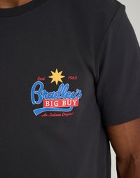 Fekete pamut póló, színes grafikával, amelyen egy sárga csillag és piros-kék felirat látható: "Bradley nagy üzlete" 1960-tól.