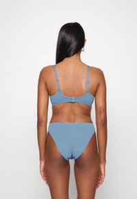 Conjunto de biquíni texturizado azul com alças ajustáveis e fecho traseiro em gancho. O top tem um design simples, combinando com as partes de baixo de cintura alta.