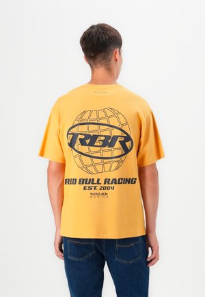 Camiseta de algodón amarilla con mangas cortas. Presenta un gran gráfico negro de un globo y el texto "RED BULL RACING EST. 2004" en la parte posterior.