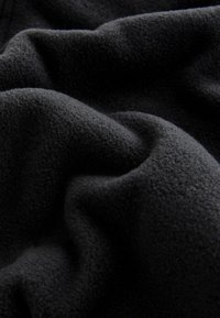 Material moale din fleece negru, cu textură vizibilă și pliuri fine ce creează o suprafață ondulată.