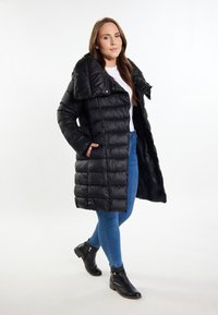Sort puffjakke med bred krave, quiltet design og sidelommer. Sammen med blå jeans og sorte ankelstøvler.