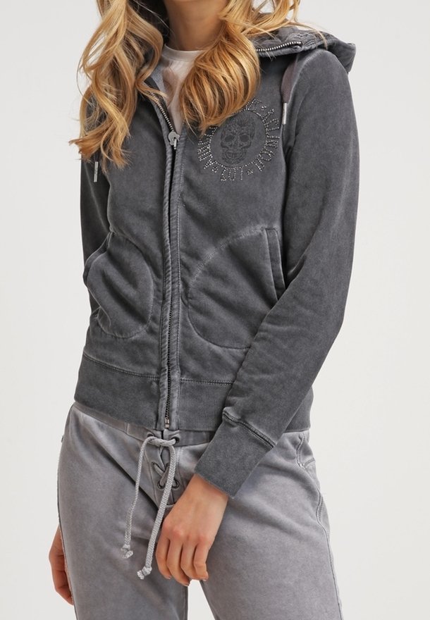 Sweat à capuche zippé gris avec une capuche, des poches avant et un graphique de crâne. Fabriqué dans un matériau doux avec une coupe décontractée et des détails à cordon.