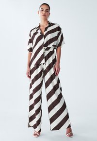 Gestreiftes Shirt in Braun und Creme, kombiniert mit weit geschnittenen Hosen aus leichtem Stoff, die einen elastischen Bund und eine entspannte Passform aufweisen.