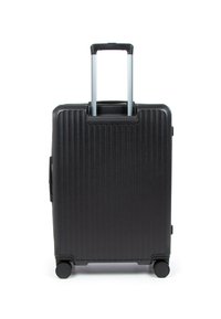 Valise rigide noire avec des rainures verticales, quatre roues et une poignée télescopique argentée extensible sur fond blanc.