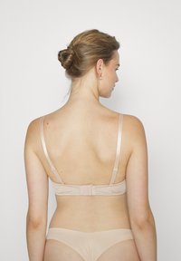 Lys beige undertøysett med en glatt stoff BH med justerbare stropper og krok-og-løkke lukking bak, kombinert med matchende truse.