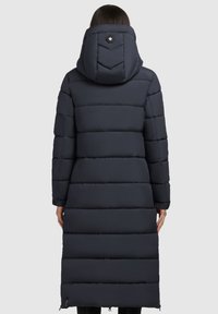 Lungo cappotto imbottito navy con cuciture orizzontali, cappuccio e polsini elastici. Presenta una chiusura con due bottoni sul cappuccio e dettagli con zip sui lati.