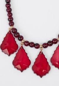 Rote Perlenkette mit drei großen, blattförmigen roten Harz-Anhängern. Glänzende Oberfläche mit goldenen Akzenten zwischen den Perlen.