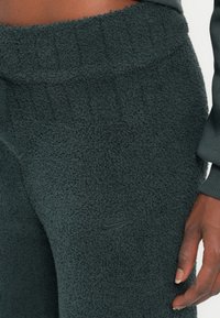 Temno sivi flis hlače z teksturirano površino in elastičnim pasom. Imajo majhen črn Nike logo na nogi.