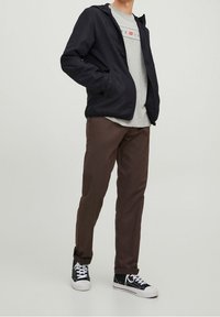Navy hooded jacket over a light gray t-shirt, brown pants, and black-and-white sneakers; jacket has two side pockets and a casual fit.