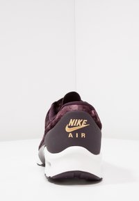 Sneaker Nike Air con una parte superiore testurizzata di colore viola scuro, branding dorato sul tallone e una suola intermedia bianca. Presenta una forma arrotondata e un design imbottito.