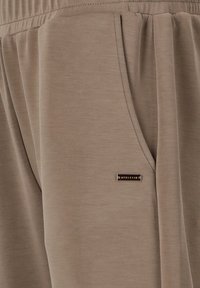 Beige joggingbroek gemaakt van zachte stof, met een elastische tailleband en zijzakken, voorzien van een klein merklabel op de voorkant.