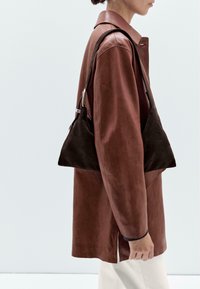 Brown leather jacket with a pointed collar and long sleeves, paired with a dark brown suede handbag featuring a triangular shape and silver accents.