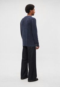 Suéter de malha canelada azul-marinho com decote redondo e mangas compridas; combinado com jeans escuros de perna larga e sapatos pretos.