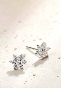Orecchini a bottone a forma di fiore in argento, caratterizzati da numerosi cristalli trasparenti tondi, montati su una base metallica lucida, su uno sfondo chiaro e texture.