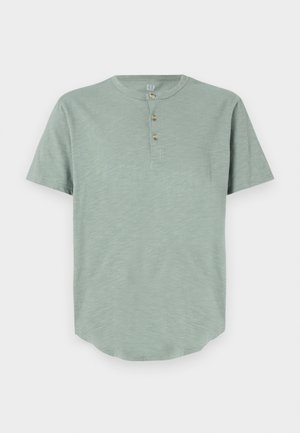 Müntroheline lühikeste varrukatega henley-särk, mis on valmistatud pehmest kangast, omades ümmargust kaelust ja kolme nupuga läbilõiget ümarate servadega.