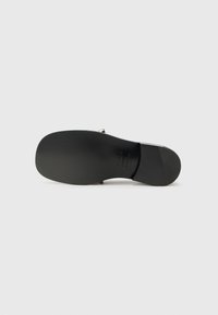Schwarze Sandale mit einer glatten, matten Oberfläche und einer stabilen flachen Sohle. Sie hat ein schlichtes Design mit minimalem Zubehör und einem einzelnen Riemen über dem Fuß.