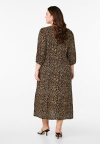 Leopardmönstrad klänning i midilängd med trekvartslånga ärmar, smal midja och flödande kjol, tillverkad av lätt material. Svarta klacksandaler.