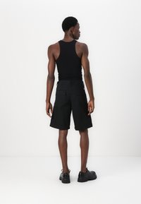Débardeur noir et shorts cargo à mi-mollet. Les shorts ont de grandes poches latérales et une coupe droite. La chaussure présente un design à semelle épaisse.