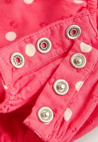 Close-up of pink fabric with white polka dots and metal snap fasteners partially connected.