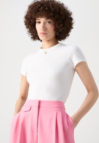 White short-sleeve top with a mock neck, made from smooth fabric. Paired with high-waisted pink pleated trousers featuring side pockets.