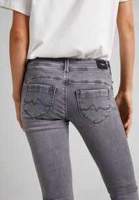 Harmaat farkut slim fit -mallissa, joissa on kaksi takataskua, sävyyn sopiva ompelu ja aaltoilevat korostukset taskuissa.