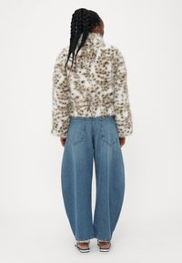 Faux pelskåpe med beige og brune leopardprikker, kombinert med vide blå jeans. Fremtredende tekstur og distinkt snitt.