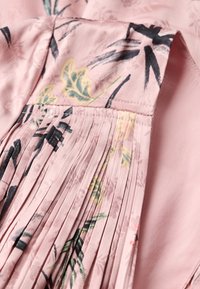 Tela rosa con pliegues, con un estampado botánico en verde y negro. Textura suave, material liviano y delicados detalles florales.