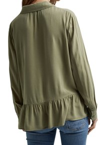 Blusa verde oliva con orlo a peplo, maniche lunghe e colletto. Texture morbida e polsini con bottoni, caratterizzata da un design fluido.