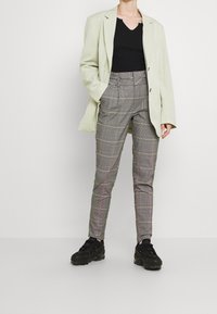 Hellgrüne oversized Blazer über einem schwarzen Top, kombiniert mit grauen Karo-Hosen mit pinken Akzenten und schwarzen Sneakers.