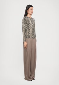 Long-sleeve top in snake print fabric with a round neckline paired with high-waisted, flowing beige trousers.