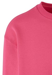 Rosa sweatshirt med rund halsringning, ribbat krage och en slät, mjuk textur. Tyget verkar lätt och bekvämt.