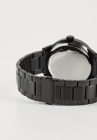 Montre en acier inoxydable noir avec un bracelet à maillons, dotée d'une lunette polie et d'un fond de boîtier rond portant le nom de la marque gravé.